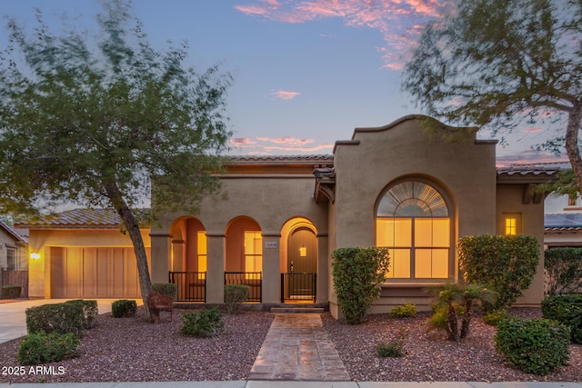 mediterranean / spanish-style home with a tile roof, an attached garage, driveway, and stucco siding