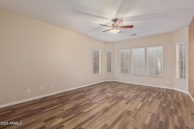 empty room featuring ceiling fan, visible vents, baseboards, and dark wood finished floors