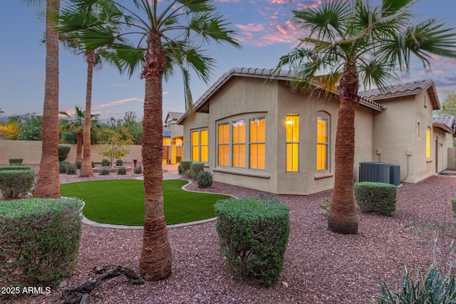 rear view of property featuring fence, central air condition unit, a tile roof, stucco siding, and a lawn