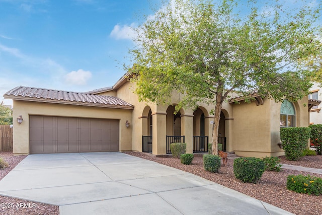 mediterranean / spanish-style home with stucco siding, a tile roof, fence, concrete driveway, and a garage