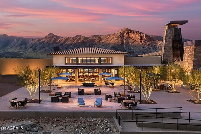 back of house at dusk featuring an outdoor hangout area, a patio area, a mountain view, and a chimney