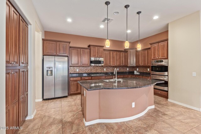 kitchen featuring visible vents, a kitchen island with sink, a sink, tasteful backsplash, and appliances with stainless steel finishes