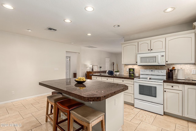 kitchen with white appliances, a breakfast bar area, backsplash, a center island, and white cabinets