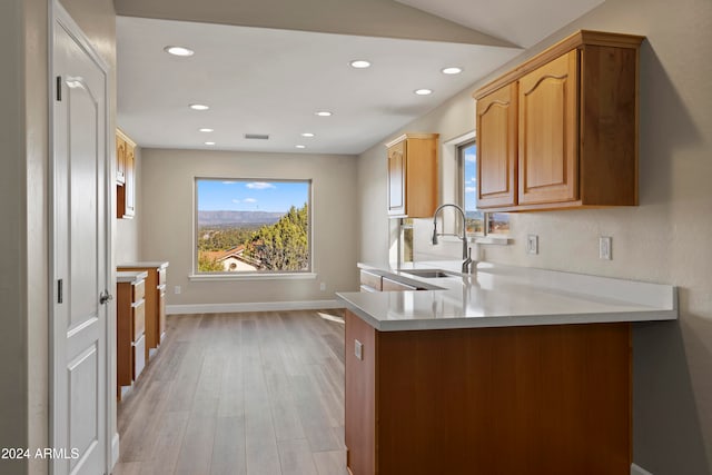 kitchen featuring kitchen peninsula, vaulted ceiling, light hardwood / wood-style flooring, and sink