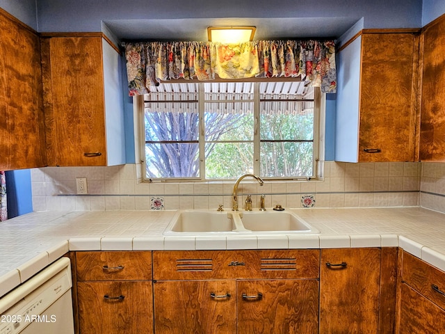 kitchen with a sink, white dishwasher, brown cabinetry, and decorative backsplash