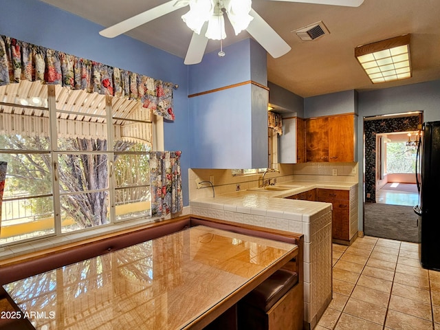 kitchen featuring a sink, tile countertops, visible vents, freestanding refrigerator, and a ceiling fan