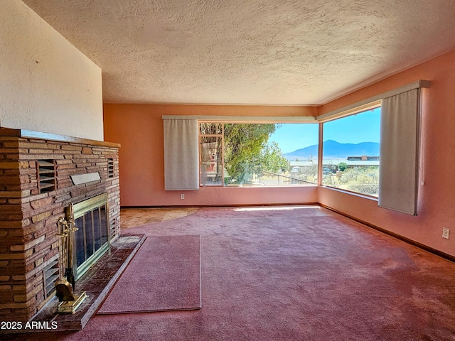 unfurnished living room with a textured ceiling, carpet, baseboards, a mountain view, and a glass covered fireplace