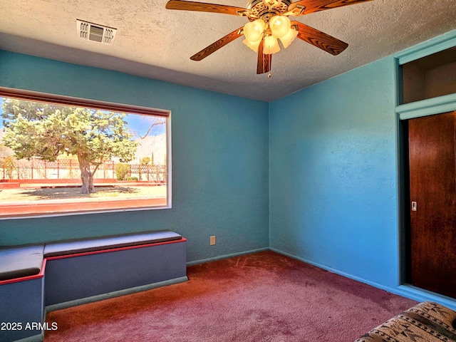 unfurnished bedroom featuring a ceiling fan, carpet, a textured ceiling, and visible vents