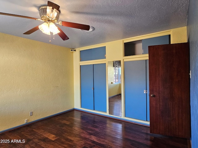 unfurnished bedroom featuring a textured ceiling, two closets, baseboards, wood finished floors, and a textured wall