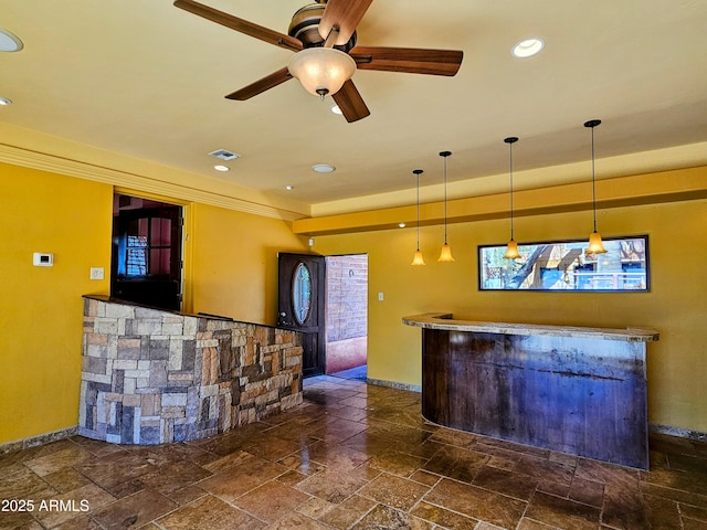 bar with a bar, a ceiling fan, stone tile flooring, and baseboards