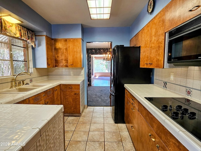 kitchen with black appliances, a sink, tile countertops, and brown cabinets