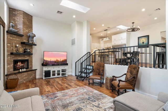 living room with a fireplace, a high ceiling, a skylight, hardwood / wood-style flooring, and a chandelier