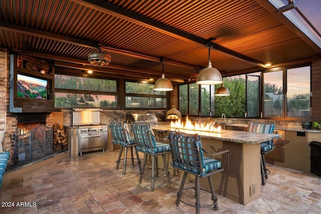 patio terrace at dusk featuring area for grilling, an outdoor bar, and exterior kitchen