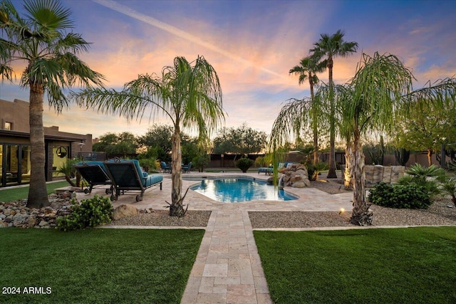 pool at dusk with a yard and a patio area