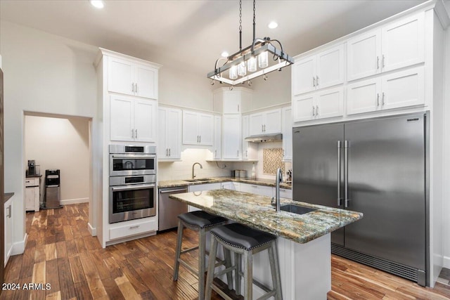 kitchen with sink, dark wood-type flooring, white cabinetry, stainless steel appliances, and dark stone countertops