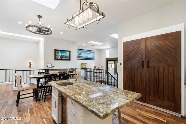 kitchen with light wood-type flooring, a center island with sink, white cabinetry, and beverage cooler