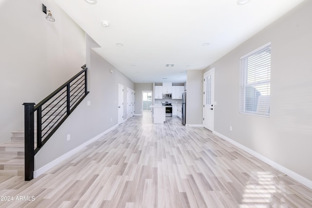 unfurnished living room featuring light wood finished floors, stairway, and baseboards