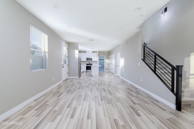 unfurnished living room with visible vents, baseboards, stairs, and light wood finished floors