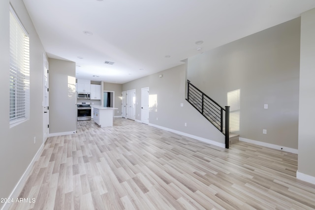 unfurnished living room with stairway, visible vents, light wood-style flooring, and baseboards