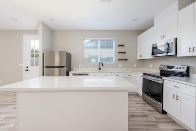 kitchen with a kitchen island, a sink, light countertops, appliances with stainless steel finishes, and white cabinetry