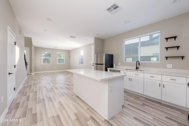 kitchen with visible vents, a sink, a kitchen island, freestanding refrigerator, and light wood-style floors