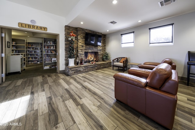 living room featuring wood-type flooring, a stone fireplace, and built in shelves