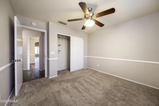 unfurnished bedroom featuring dark colored carpet, ceiling fan, and a closet