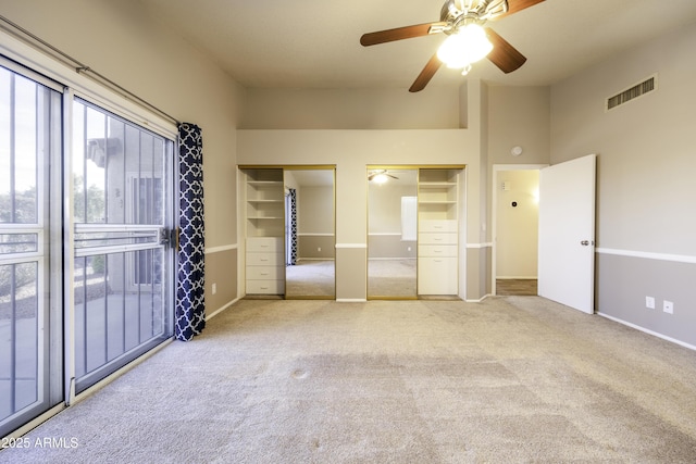 unfurnished bedroom featuring ceiling fan, light carpet, a high ceiling, and multiple closets