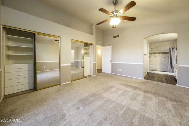 unfurnished bedroom featuring carpet flooring, ensuite bath, ceiling fan, and multiple closets