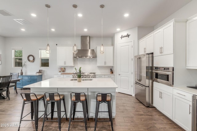 9764 E Thornbush Ave, Mesa, AZ 85212 - kitchen featuring wall chimney range hood, stainless steel appliances, a breakfast bar, backsplash, and white cabinets