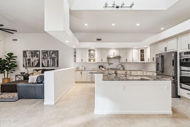 kitchen featuring sink, dark stone counters, light tile patterned floors, stainless steel appliances, and a spacious island