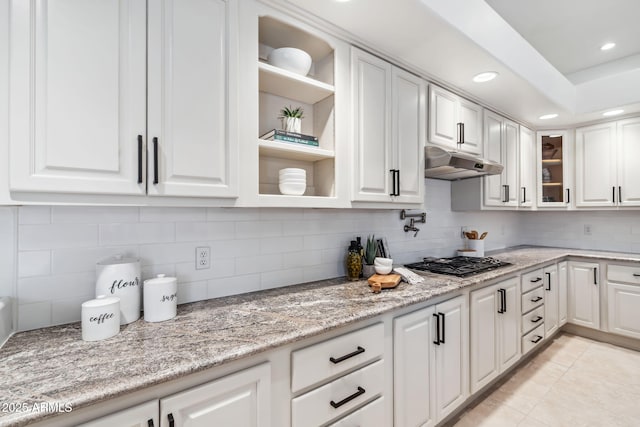 kitchen with light tile patterned floors, backsplash, light stone counters, gas stovetop, and white cabinets