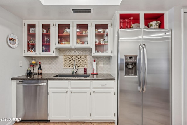 kitchen featuring visible vents, a sink, tasteful backsplash, stainless steel appliances, and glass insert cabinets