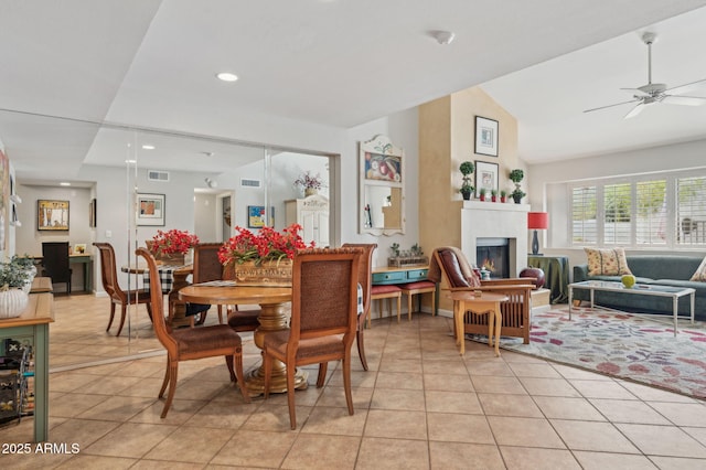 dining area featuring lofted ceiling, light tile patterned floors, visible vents, and a warm lit fireplace