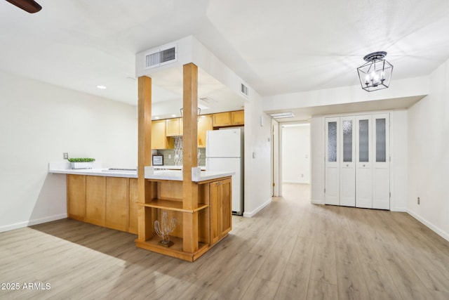 kitchen featuring visible vents, light wood-style flooring, freestanding refrigerator, a peninsula, and light countertops