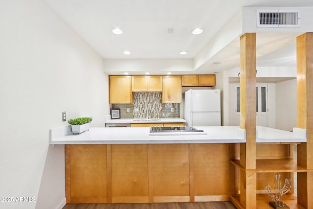 kitchen featuring black electric stovetop, tasteful backsplash, visible vents, freestanding refrigerator, and a peninsula