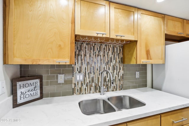 kitchen with light brown cabinetry, backsplash, a sink, and light stone countertops