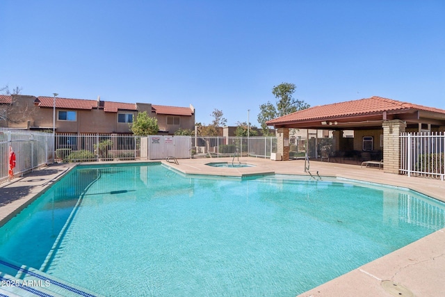 community pool with a patio, fence, and a hot tub