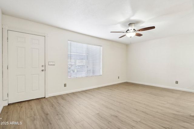 spare room featuring light wood finished floors, a ceiling fan, and baseboards