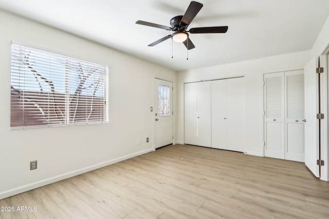 unfurnished bedroom featuring baseboards, ceiling fan, light wood finished floors, and two closets