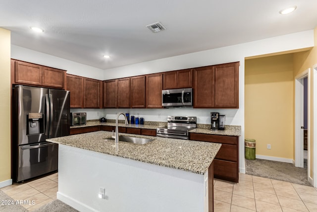 kitchen featuring light stone countertops, sink, an island with sink, light tile patterned floors, and appliances with stainless steel finishes