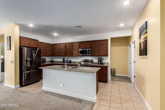 kitchen featuring light stone countertops, sink, stainless steel appliances, light carpet, and a kitchen island with sink