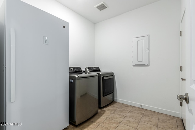 clothes washing area with electric panel, washer and clothes dryer, and light tile patterned floors