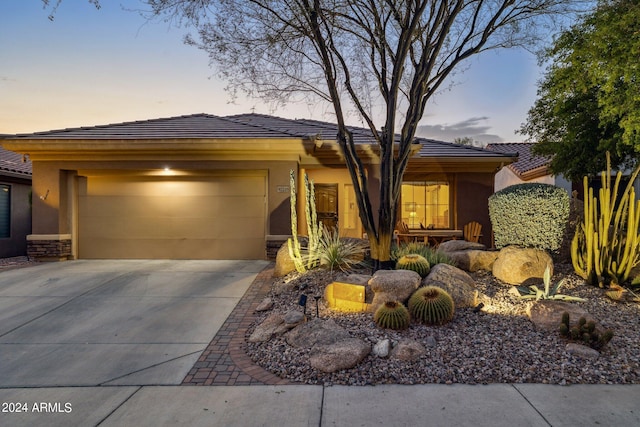 view of front facade featuring driveway, stone siding, an attached garage, and stucco siding