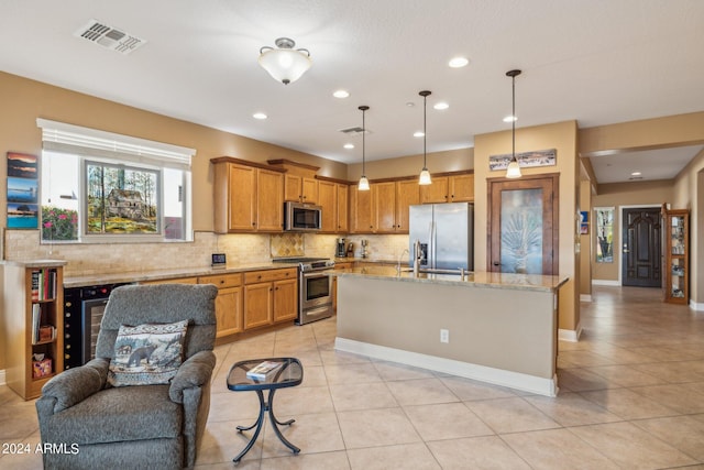 kitchen with stainless steel appliances, a center island with sink, light tile patterned floors, decorative light fixtures, and light stone countertops