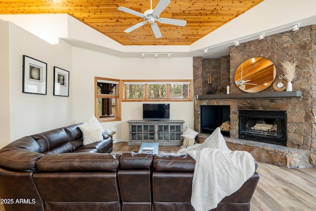 living room with a ceiling fan, wood ceiling, wood finished floors, vaulted ceiling, and a stone fireplace