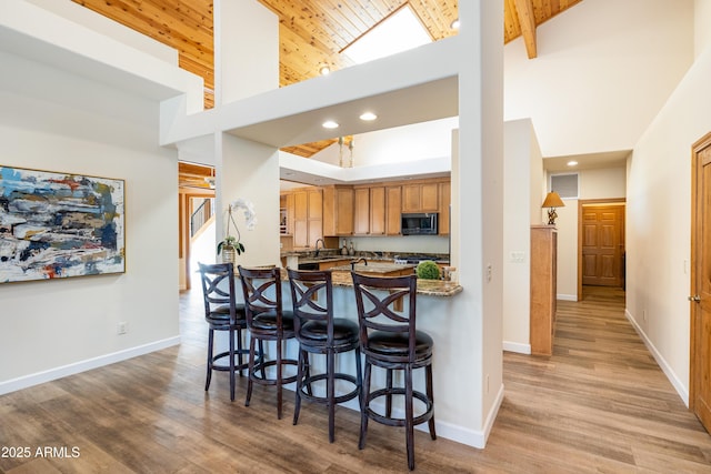 kitchen with high vaulted ceiling, wood finished floors, baseboards, stainless steel microwave, and a kitchen bar