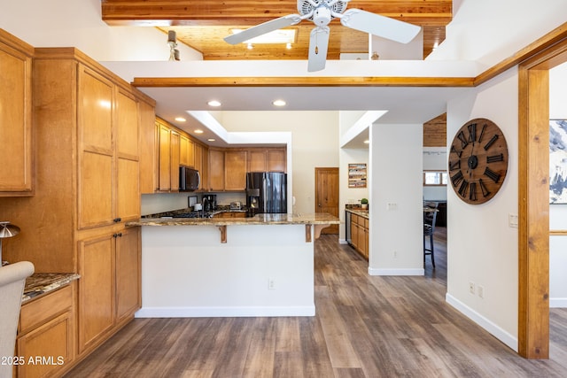 kitchen featuring black microwave, stone counters, a peninsula, stainless steel fridge, and a kitchen bar