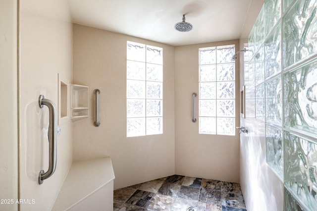 full bath featuring a wealth of natural light, stone finish flooring, and walk in shower