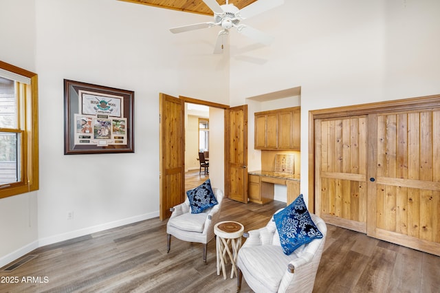 living area featuring visible vents, a high ceiling, a ceiling fan, wood finished floors, and baseboards